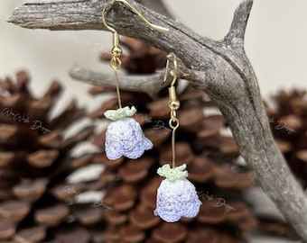 May include: A pair of delicate crocheted flower earrings with a light purple and green color gradient. The earrings are hanging from gold hooks.