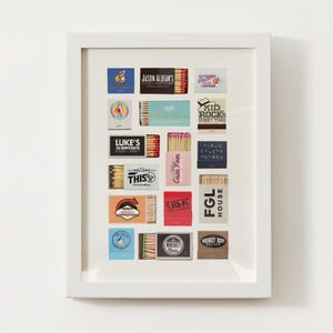 May include: A white frame with a white mat surrounding a collection of 18 matchboxes with various designs. The matchboxes feature logos and text, including "Jason Aldean's", "Kid Rock", "Luke's 32 Bridge", "FGL House", "Whiskey Bent", and "Casa Pava".