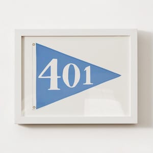 May include: A framed print showing a blue pennant with the white number "401". The pennant is set against a white background and enclosed in a white frame. The artwork is simple and clean, suitable for nautical or minimalist decor.