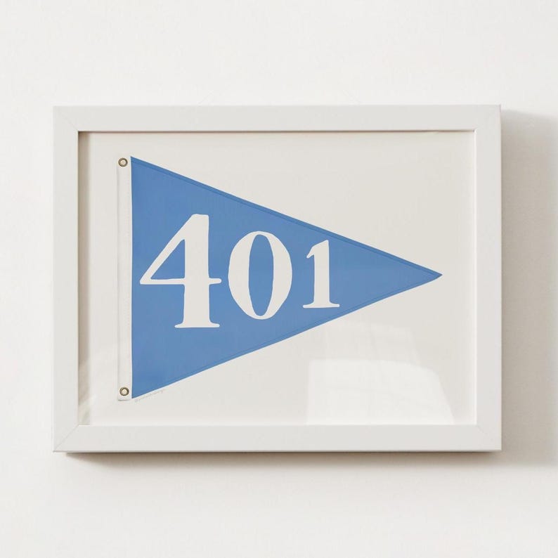 May include: A framed print showing a blue pennant with the white number "401". The pennant is set against a white background and enclosed in a white frame. The artwork is simple and clean, suitable for nautical or minimalist decor.