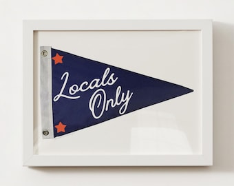 May include: A framed print of a blue pennant with white text that reads "Locals Only". The pennant has two red stars on it.