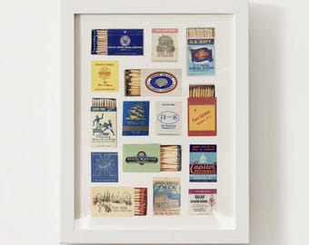 May include: A framed collection of vintage matchbooks, showcasing various designs and logos. The matchbooks are arranged in a grid pattern within a white frame, offering a glimpse into historical branding and design.