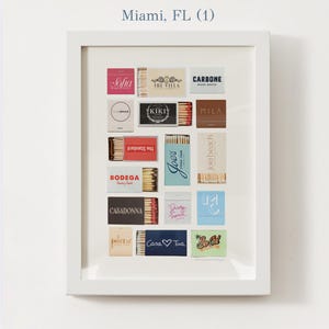 May include: A white framed print of a collection of matchboxes with various names and logos, including "Sofia", "The Villa", "Carbone", "Space", "Kiki", "Mila", "The Standard", "Joe's", "Bodega", "Casadonna", "Dirty French", "Jola Beach", "Paleme", "Casa Tua", and "So Old". The print is titled "Miami, FL (1)".