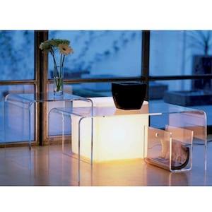 以下が含まれることがあります： 丸みを帯びたエッジを持つ、透明なアクリル製の入れ子式テーブル3つ。テーブルは、後ろに最も大きく、前に最も小さいテーブルが配置された、段差のある配置になっています。黒いボウルが上のテーブルに置かれ、雑誌ラックが下のテーブルに取り付けられています。