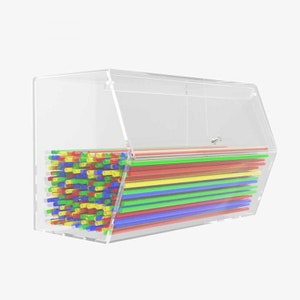 Può includere: Un distributore in acrilico trasparente riempito di cannucce di plastica colorate. Il distributore ha un coperchio incernierato e uno slot per erogare le cannucce.
