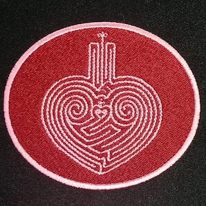 May include: A circular embroidered patch with a red background and a white heart-shaped maze design. The patch has a pink border and a stylized top element. The design is centered on a black background.