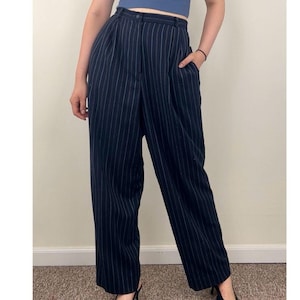 May include: Black pinstripe trousers with a high waist and a straight leg. The pants have a button closure and pockets. The pinstripes are a light color against the dark background. The trousers are a classic style.