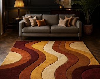 May include: A large, retro-style area rug with a wavy pattern in shades of burgundy, orange, yellow, and cream. The rug is placed in a living room with a gray sofa and a dark wall. The rug's dimensions are not visible.