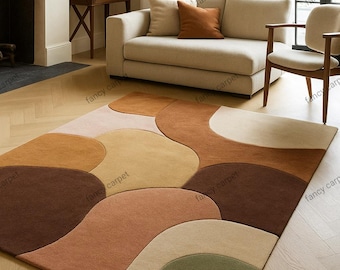 May include: A large, abstract area rug with a flowing, organic design. The rug features a palette of warm, earthy tones, including shades of brown, beige, and olive green. The rug is placed on a hardwood floor, and is in a living room setting.