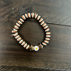 May include: A bracelet made of black, white, and orange striped beads with gold star charms and a gold heart charm.