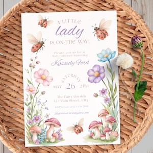 Peut inclure: Une invitation à une baby shower avec des illustrations à l'aquarelle de coccinelles, de champignons et de fleurs. L'invitation indique "A Little Lady Is On The Way !" et comprend les détails de l'événement. L'invitation est posée sur un panier tressé.