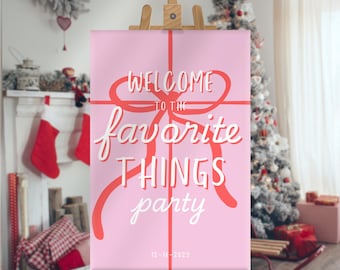 May include: A pink sign on a wooden easel with the words "WELCOME TO THE favorite THINGS party" in white and red script. The sign is decorated with a red bow and the date 12-18-2025. A Christmas tree and decorations are in the background.