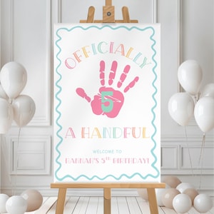 May include: A white sign on a wooden easel with the text "OFFICIALLY 5 A HANDFUL" in colorful letters. A pink handprint with a teal "5" is in the center. The sign reads "WELCOME TO HANNAH'S 5TH BIRTHDAY!" and is surrounded by white balloons.