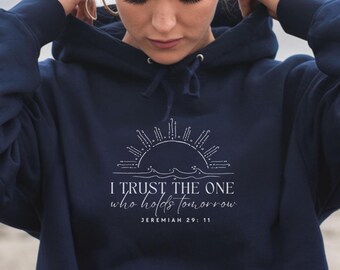 May include: Navy blue hoodie with a white graphic of a sun over waves and the text "I TRUST THE ONE who holds tomorrow" from Jeremiah 29:11. The hoodie has a drawstring hood and a front pocket.