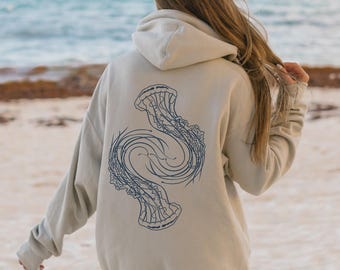 Peut inclure: Un sweat à capuche beige clair avec un motif de méduse bleu au dos. Le motif de la méduse est une illustration stylisée avec des lignes fluides. Le sweat à capuche est un vêtement décontracté, idéal pour un usage quotidien.