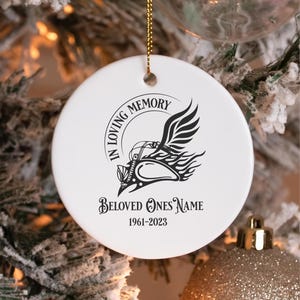 Può includere: Ornamento natalizio in ceramica bianca con un design di motocicletta nera e le parole "IN LOVING MEMORY" e "BELOVED ONES NAME 1961-2023". L'ornamento ha un cordino dorato per appenderlo.
