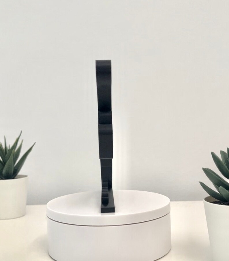 May include: A black, freestanding, three-dimensional letter "S" made of acrylic. The letter is standing on a white circular base.