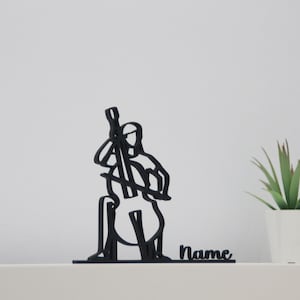 Puede incluir: Silueta negra de una persona tocando un violonchelo, con la palabra "Name" debajo. La silueta está sobre una superficie blanca con una planta verde en una maceta blanca a la derecha.