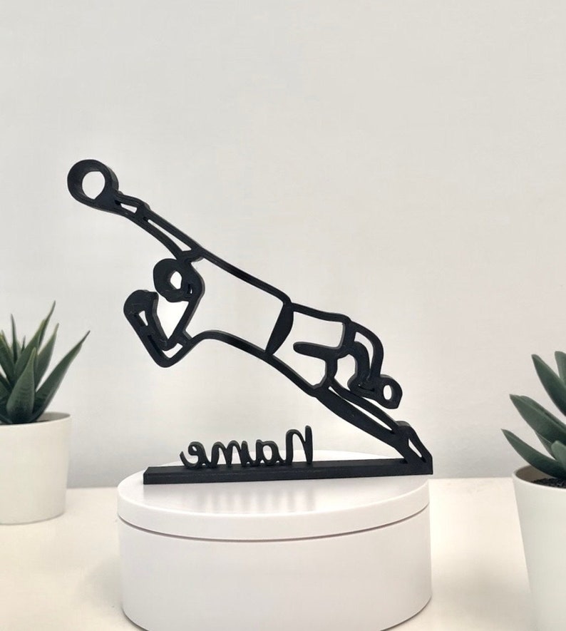 May include: Black silhouette of a soccer player diving to save a ball, with the word "Name" written on a base.