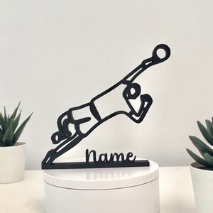 May include: Black silhouette of a soccer player diving to save a ball, with the word "Name" on a base.