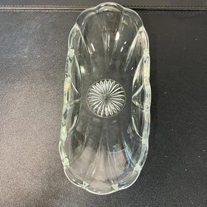 May include: A clear glass dish with a scalloped rim and a starburst design in the center. The dish is oblong and has a textured, ribbed pattern on the sides.