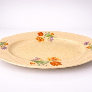 May include: Cream-coloured oval serving platter with a textured rim. The platter features floral designs in orange, purple, and green. A vintage piece, suitable for serving appetizers or desserts.