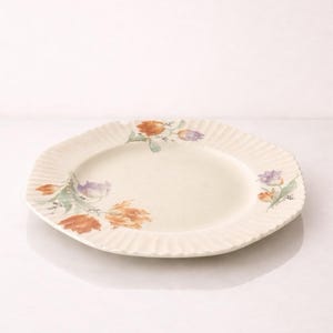 Puede incluir: Plato ovalado de servir de color crema con borde ondulado. El plato está decorado con diseños florales en acuarela naranja, morado y verde. Una pieza decorativa para servir alimentos.