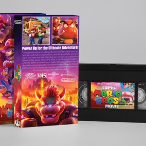 May include: The Super Mario Bros. Movie VHS tape and two matching boxes. The boxes feature colorful illustrations of Mario, Luigi, and Bowser. The VHS tape has a matching label. The text "Power Up for the Ultimate Adventure!" is visible.