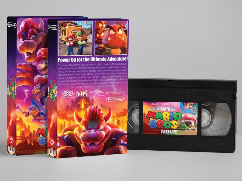 May include: The Super Mario Bros. Movie VHS tape and two matching boxes. The boxes feature colorful illustrations of Mario, Luigi, and Bowser. The VHS tape has a matching label. The text "Power Up for the Ultimate Adventure!" is visible.
