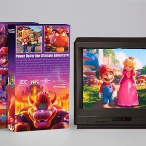 May include: A VHS tape box and a television displaying a scene from the Super Mario Bros. movie. The box is purple and features Bowser and other characters. The TV shows Mario and Princess Peach in a colorful mushroom kingdom.
