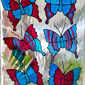 May include: Six colorful butterfly decorations with a stained glass effect. The butterflies have blue and red wings with intricate patterns. The background is a textured, reflective surface.