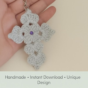 May include: A crocheted cross keychain in light gray, featuring a purple center bead. The image includes the text "CROCHET CROSS KEYCHAIN" and "PDF PATTERN &bull; English Tutorial". Additional text reads "Handmade &bull; Instant Download &bull; Unique Design".