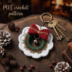 May include: A handmade crochet wreath keychain with a red bow, green wreath, and gold accents. The keychain includes a small silver bell and a set of keys. The text "PDF crochet pattern" is visible in the image.