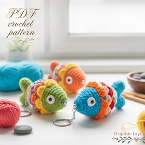 Peut inclure: Trois porte-clés en forme de poissons crochetés aux couleurs vives : vert, orange et bleu, avec des nageoires arc-en-ciel. L'image affiche également de la laine et le texte "PDF crochet pattern".