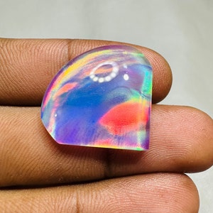 May include: A cabochon cut iridescent opal gemstone with a rainbow of colors, including pink, blue, green, and purple. The opal is set in a clear, faceted setting.