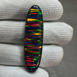 May include: A black oval opal cabochon with iridescent rainbow stripes. The opal is set in a clear epoxy.
