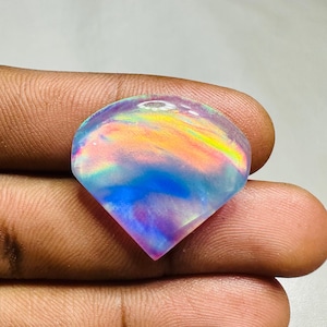 May include: A teardrop-shaped iridescent opal gemstone with a rainbow of colors, including pink, blue, yellow, and green.