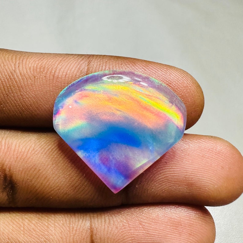 May include: A teardrop-shaped iridescent opal gemstone with a rainbow of colors, including pink, blue, yellow, and green.