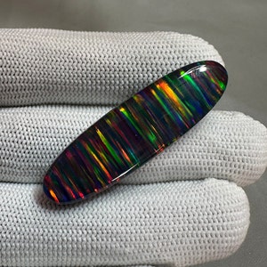 May include: A black opal cabochon with a striated pattern of iridescent colors, including green, red, and blue.