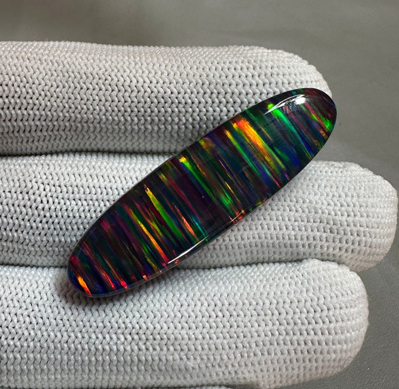 May include: A black opal cabochon with a striated pattern of iridescent colors, including green, red, and blue.