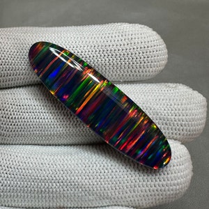 May include: A black opal cabochon with a striated pattern of iridescent colors, including red, orange, yellow, green, blue, and purple.