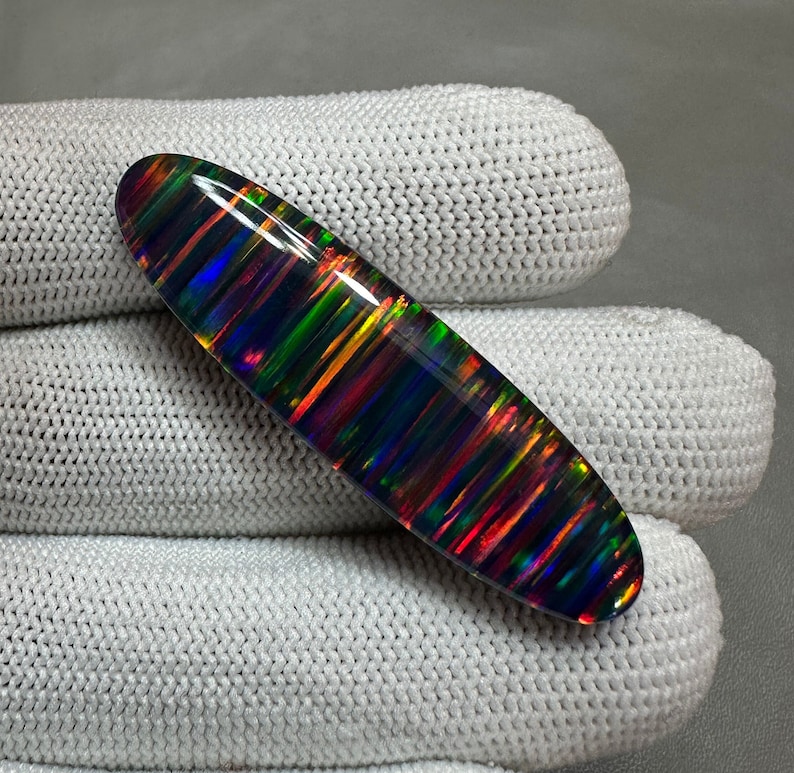 May include: A black opal cabochon with a striated pattern of iridescent colors, including red, orange, yellow, green, blue, and purple.
