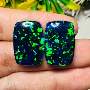 May include: Two rectangular, polished gemstones with a dark blue base and vibrant green and blue inclusions. The stones have rounded corners and a glossy finish, showcasing a play of color. These opals are ideal for jewelry making.