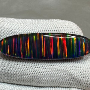 May include: A black oval opal gemstone with iridescent streaks of red, orange, yellow, green, blue, and purple.