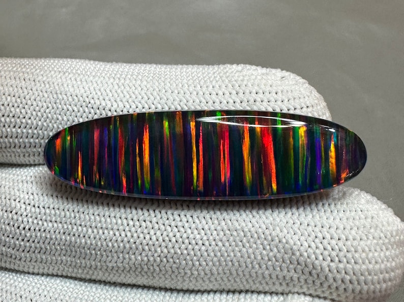May include: A black oval opal gemstone with iridescent streaks of red, orange, yellow, green, blue, and purple.