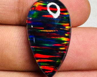 May include: A teardrop-shaped black opal gemstone with vibrant red, green, and yellow flashes. The polished stone has a glossy surface and a unique pattern of color bands. The opal is held between fingers.