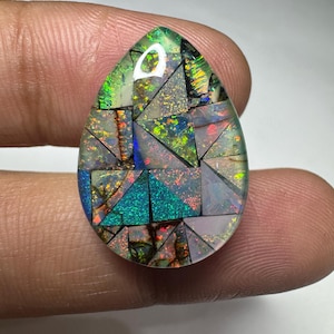 May include: A teardrop-shaped mosaic gemstone featuring a variety of triangular and irregular fragments. The stone displays a vibrant play of color with iridescent flashes of green, blue, orange, and red set against a dark, semi-translucent base.