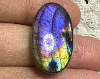 Op de afbeelding: Ovaalvormige labradorit edelsteen cabochon met iriserende paarse, blauwe en gele kleuren.