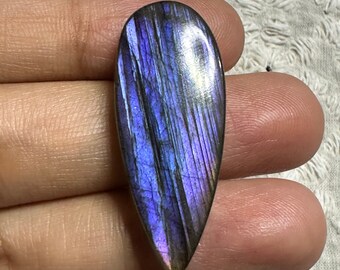 Op de afbeelding: Een traanvormige labradorit-cabochon met iriserende blauwe, paarse en zwarte kleuren.