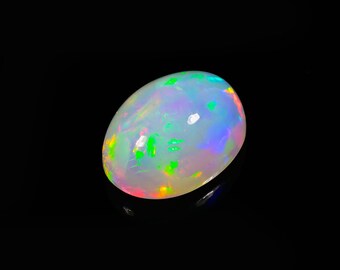 Può includere: Una gemma di opale lucidata, di forma ovale. L'opale mostra un colore di base bianco latte con lampi iridescenti di verde, blu e rosso. La gemma è posta su uno sfondo nero, evidenziando il suo vibrante gioco di colori.